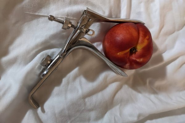 Speculum holding a nectarine on a white background