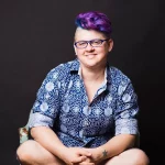 white, nonbinary person, Frances Reed, sitting crosslegged on a chair