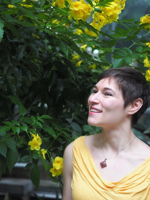 Bianca in a yellow blouse standing in a garden, looking to the left